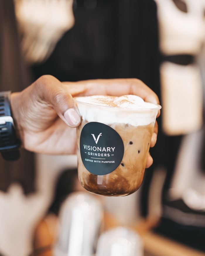 Hand holding a layered iced latte topped with cold foam