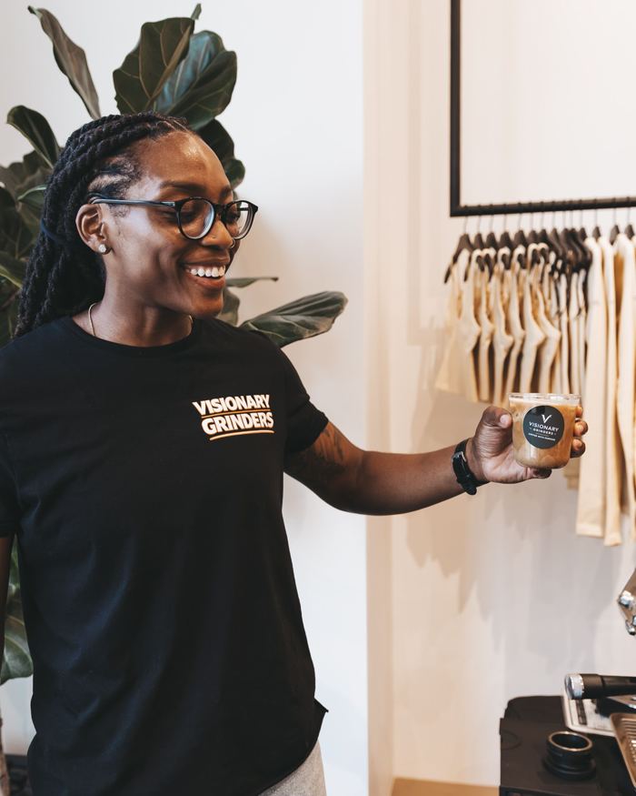 Jasmine Rhodes smiling while holding a Visionary Grinders iced latte at a pop-up